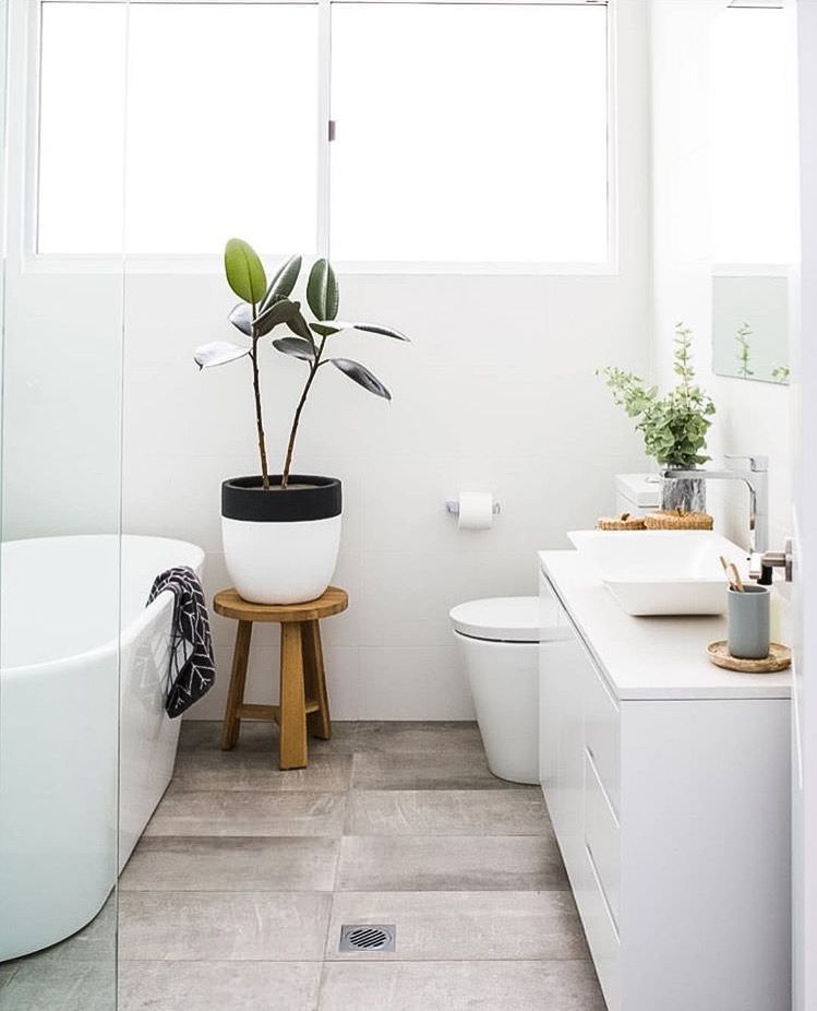 حمام و سرویس بهداشتی مدرن با وان و روشویی سفید و کفپوش وینیل که برای جذب انرژی مثبت از گیاه در آن استفاده شده است
